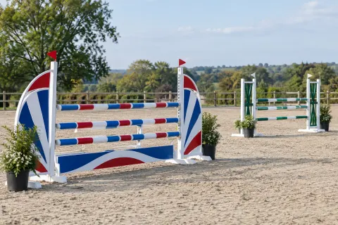 An empty showjumping course of painted poles and wings in a sand arena.